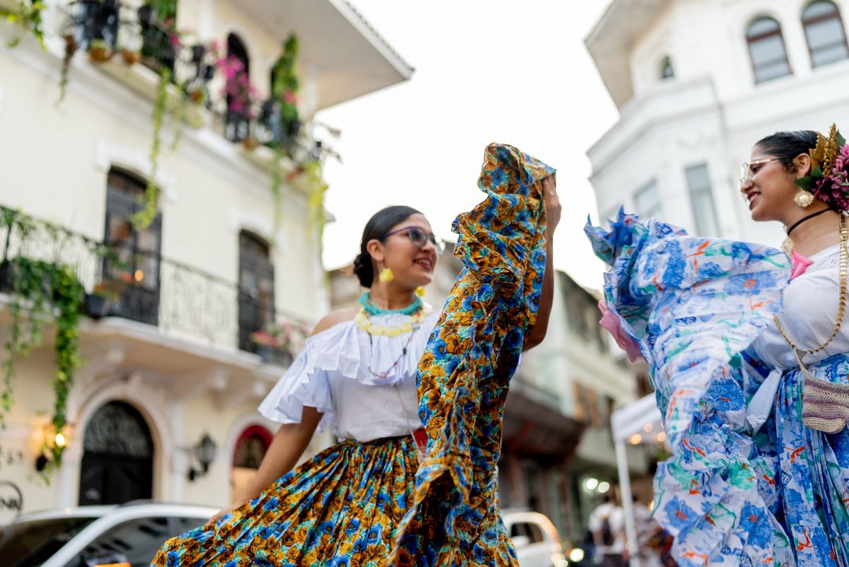 Two women in traditional pollera dresses dancing in a street in Panama City's old quarter