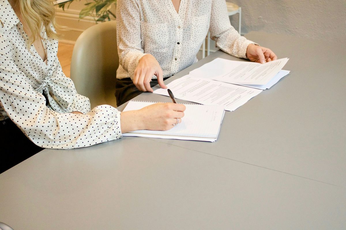 Two people at a table, one signing a document